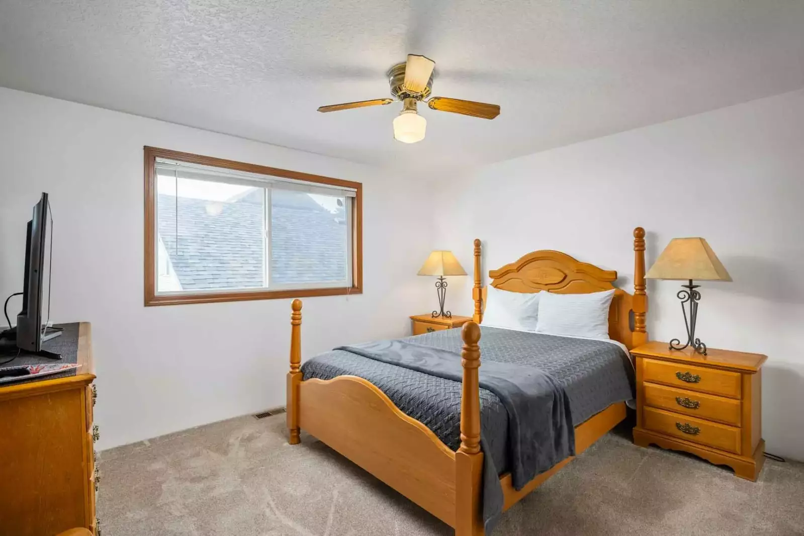 This comfy bedroom has a smart tv and a ceiling fan.