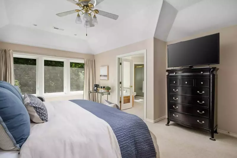 This bedroom features an en suite bathroom, ceiling fan, comfy bed, and smart tv.