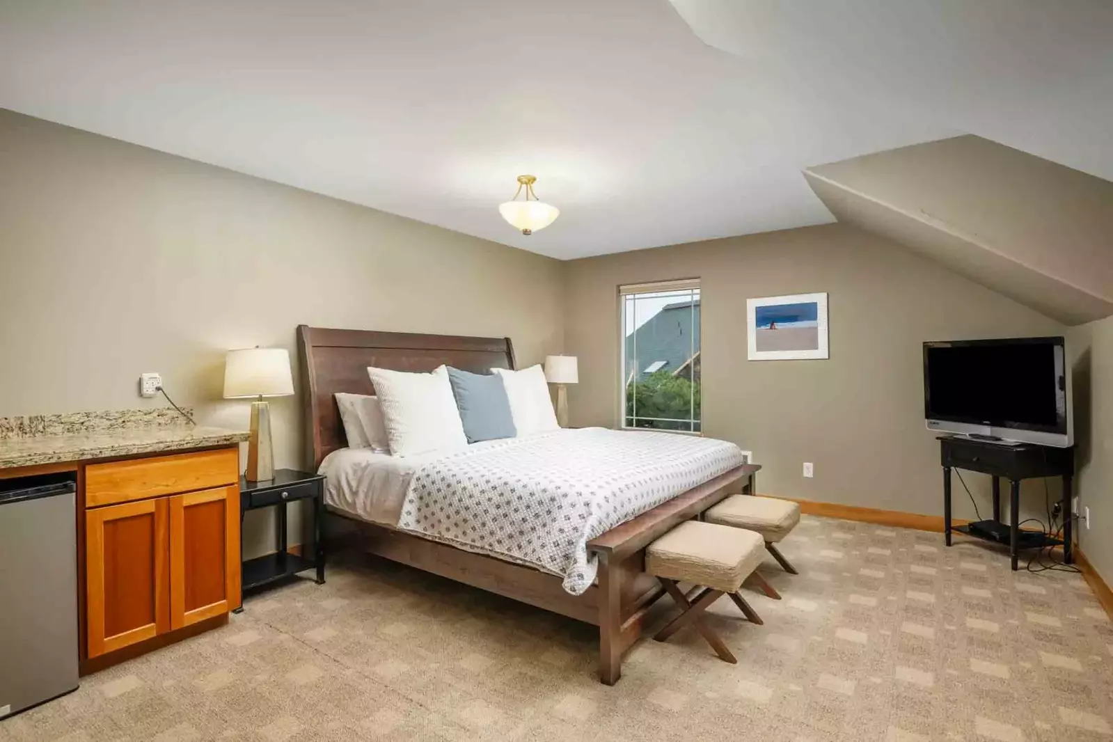 This bedroom has a tv, a minifridge, a king bed, and lots of space.