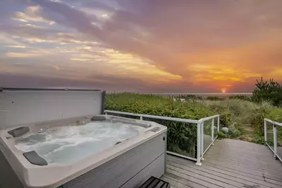 Walk right out to an expansive deck with a hot tub, dining tables, a gas barbecue, and a private entrance to a sandy path to miles of beach.