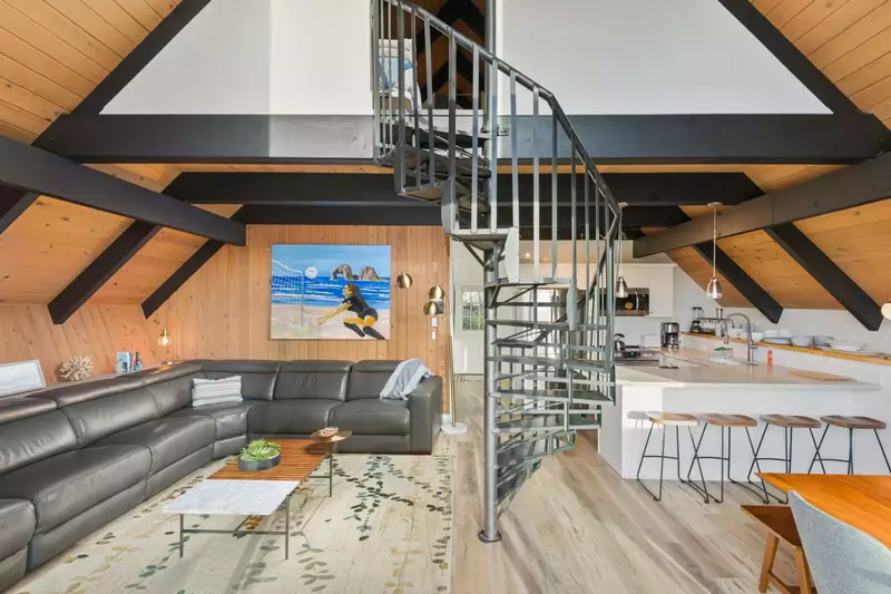 Open-concept living space features a spacious corner couch, flat screen TV, and handsome spiral staircase leading up to the lofted sleeping quarters.