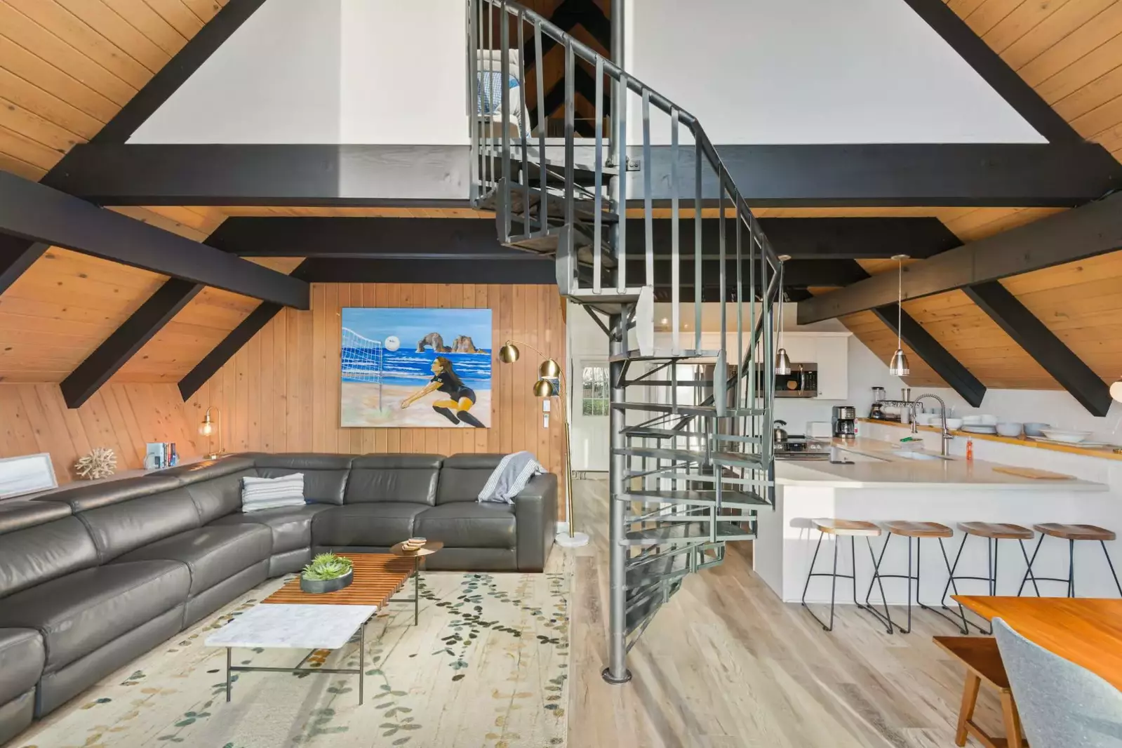 Open-concept living space features a spacious corner couch, flat screen TV, and handsome spiral staircase leading up to the lofted sleeping quarters.