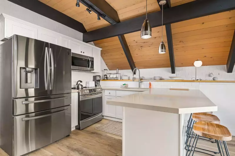 Full kitchen dressed in stainless steel appliances that include a French door refrigerator, dishwasher & even a breakfast bar with four barstools.
