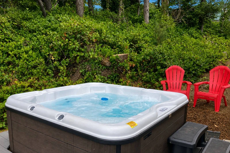 A bubbling outdoor hot tub surrounded by greenery and classic Adirondack chairs.